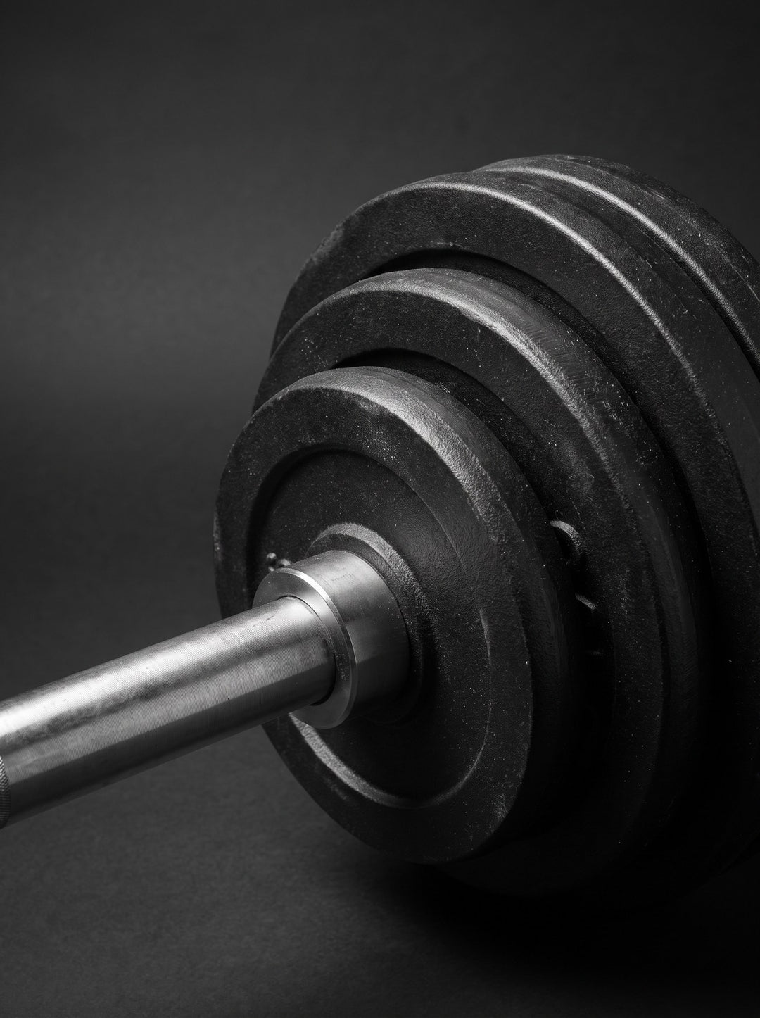 Close-up of a barbell with stacked black iron plates photographed as a sculptural still life in black, grey and silver